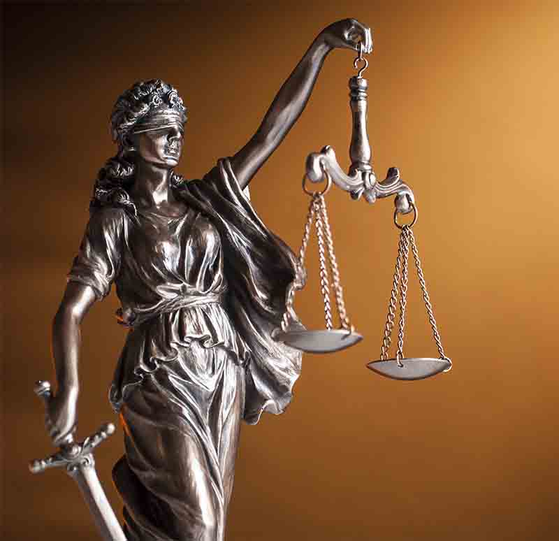 Bronze statue of Justice carrying a sword and holding up scales representing law and order over a brown background with copy space